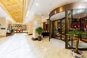 Un hall d’hôtel avec un comptoir d’accueil, une grande plante et un mur incurvé en verre.