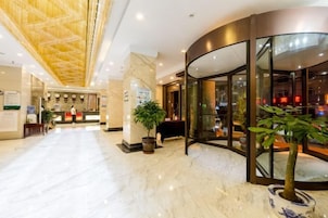 Un vestíbulo de hotel con una recepción, una planta grande y un muro de cristal curvo.