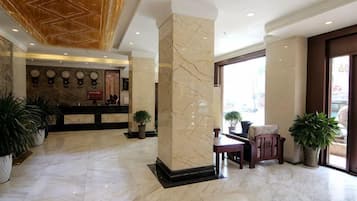 A hotel lobby with marble flooring, a reception desk, and potted plants.