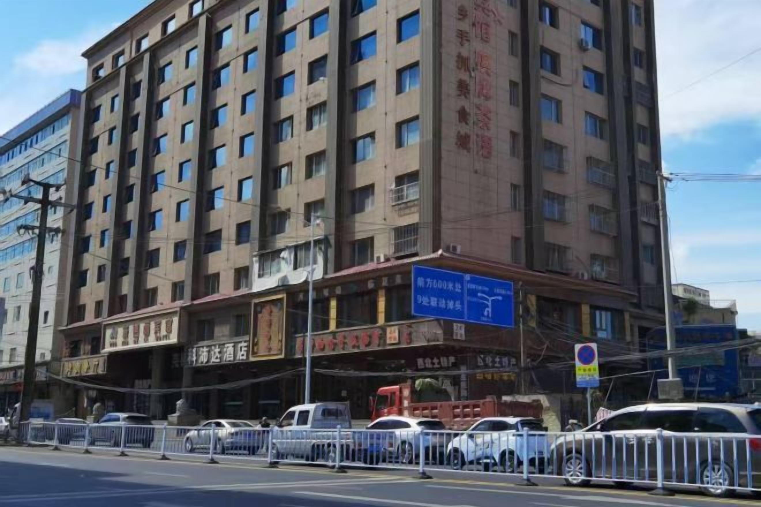 Ένα πολυώροφο ξενοδοχείο με μια μεγάλη επιγραφή, πολλά παράθυρα και έναν περιφραγμένο χώρο στάθμευσης.