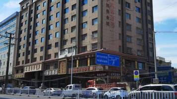 A multi-story hotel with a large signboard, multiple windows, and a fenced parking area.