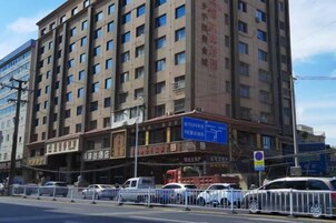 A multi-story hotel with a large signboard, multiple windows, and a fenced parking area.