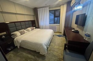 Habitación de hotel con una cama grande, un escritorio, una silla, un televisor y una ventana con cortinas.