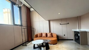 Ein modernes Wohnzimmer mit einer Couch, einem runden Couchtisch, einer Waschmaschine und einem großen Fenster.