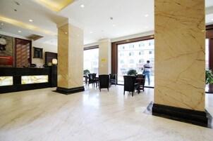A hotel lobby with marble flooring, a reception desk, and seating area.