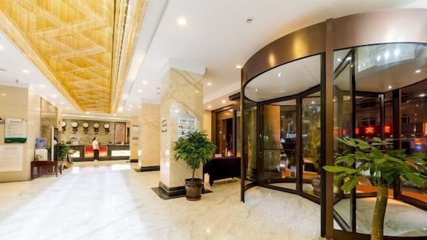 Eine Hotelhalle mit Marmorboden, einer Rezeption, einem gebogenen Glaseingang und Topfpflanzen.