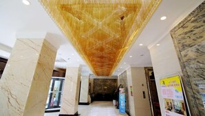 Eine Hotelhalle mit einem geometrisch gemusterten Decken, Marmorkolonnen und einem Empfangsbereich.