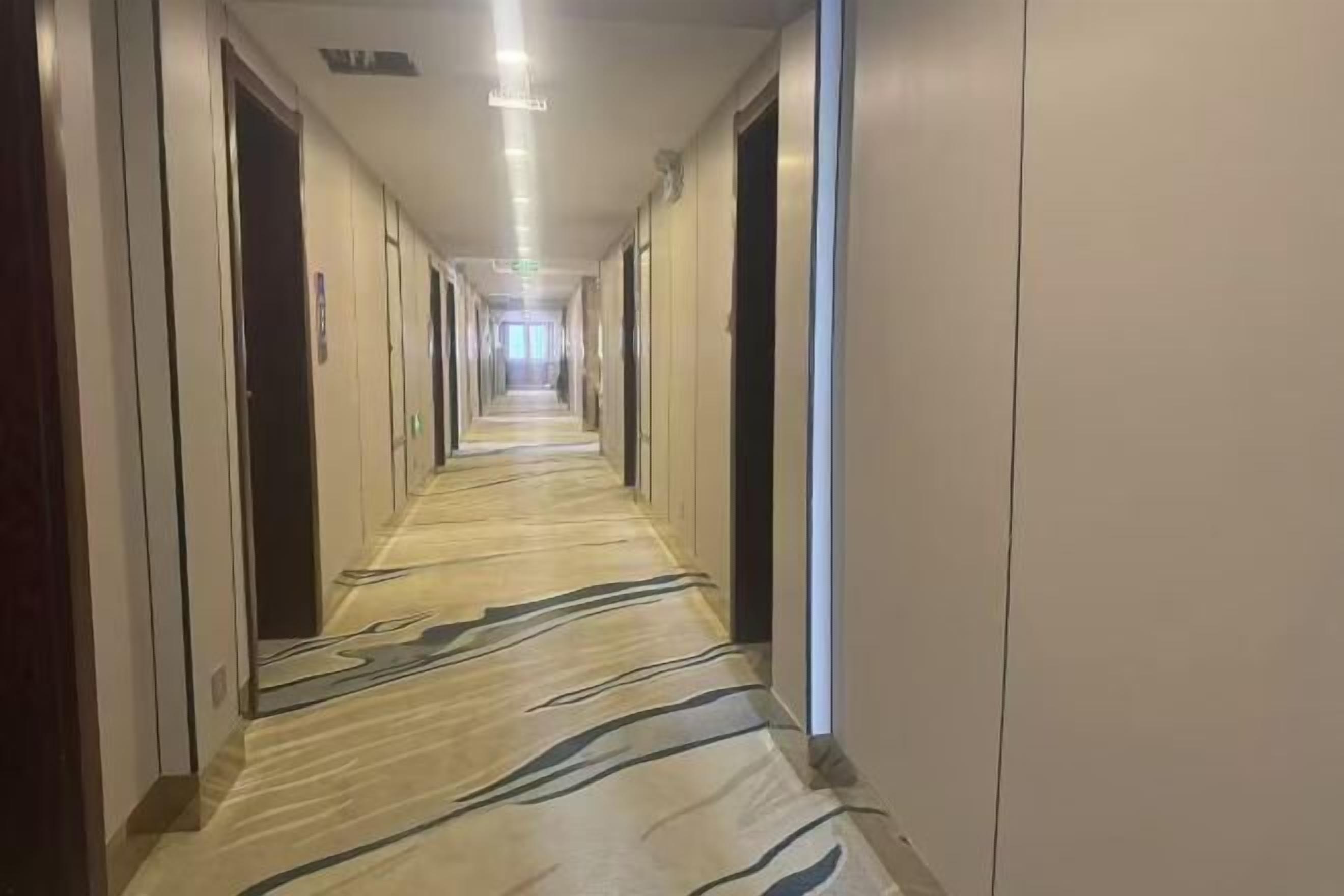 A long, narrow hotel corridor with doors on both sides and a patterned carpet.