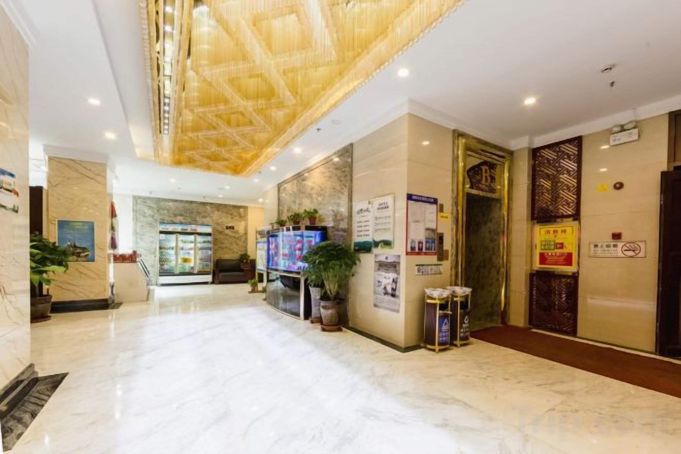 Un vestíbulo de hotel con suelo de mármol, un mostrador de recepción y una escalera que sube a los pisos superiores.