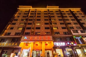 Un hôtel à plusieurs étages, doté d’une enseigne lumineuse et de nombreux commerces situés au rez-de-chaussée.