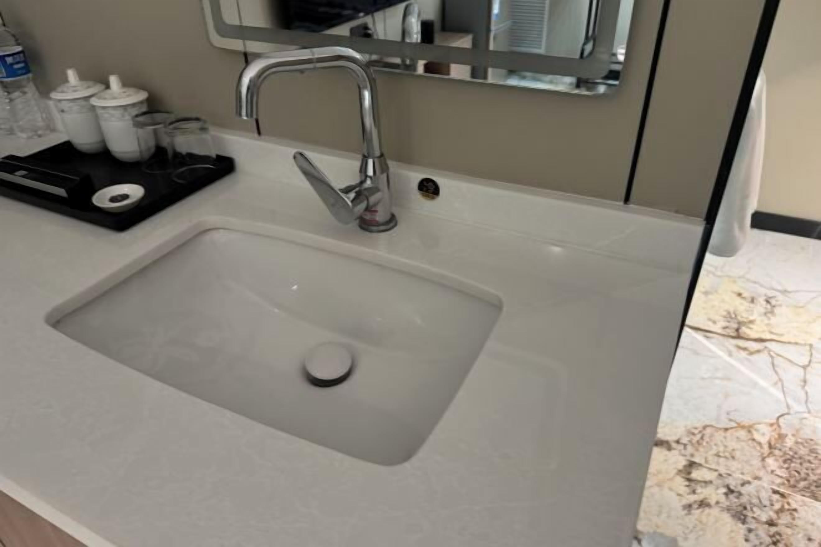 A bathroom sink with a modern faucet, a mirror above it, and toiletries on a tray.