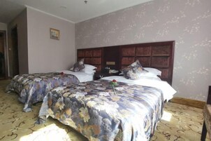 Una habitación de hotel con dos camas, cubrecamas florales, un cabecero de madera y una alfombra estampada.