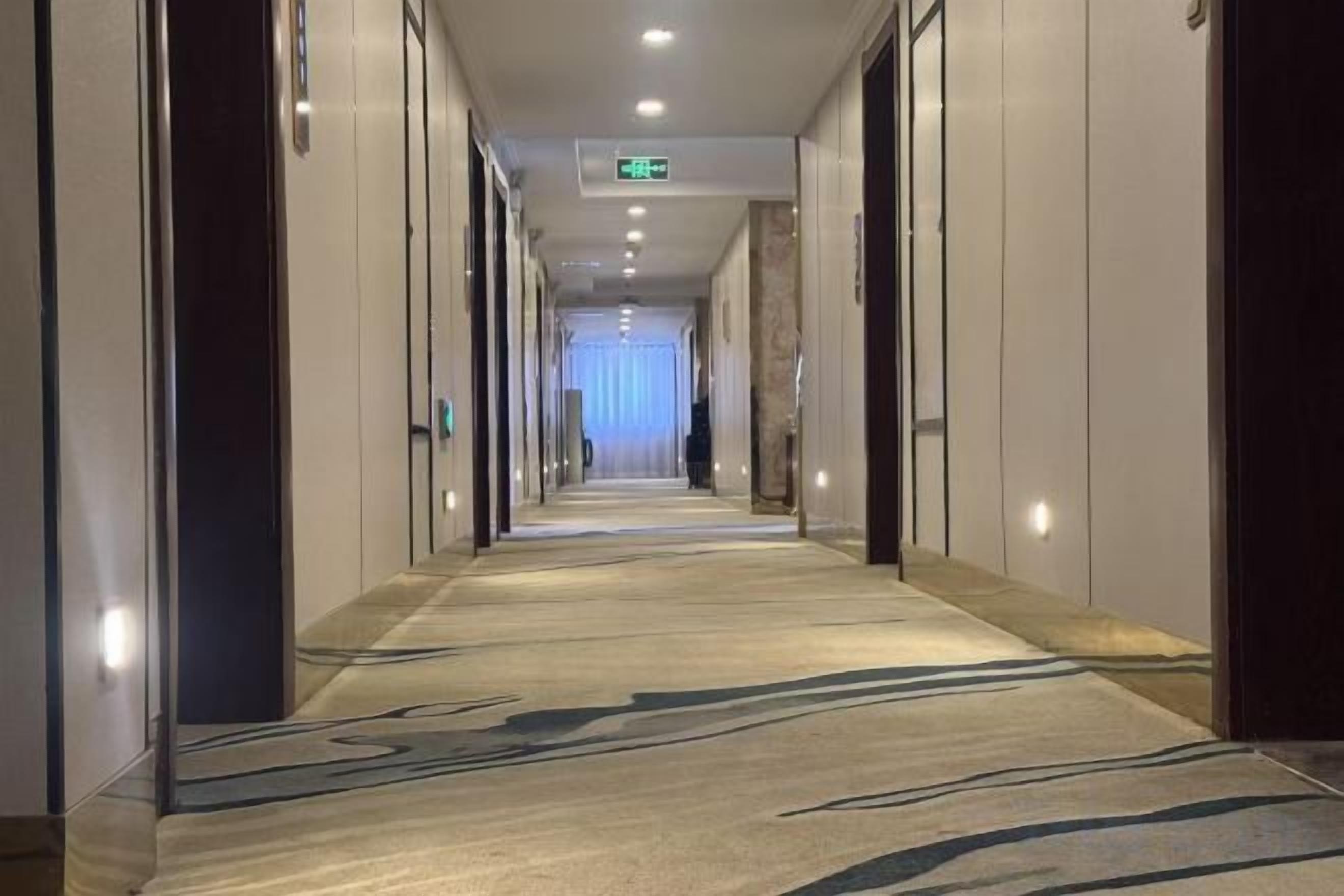 A hotel corridor with a carpeted floor, doors on both sides, and a light source at the end.