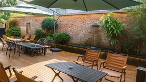 Eine Terrasse im Freien mit Holztischen und -stühlen, Sonnenschirmen und einer Backsteinwand mit Grünpflanzen.