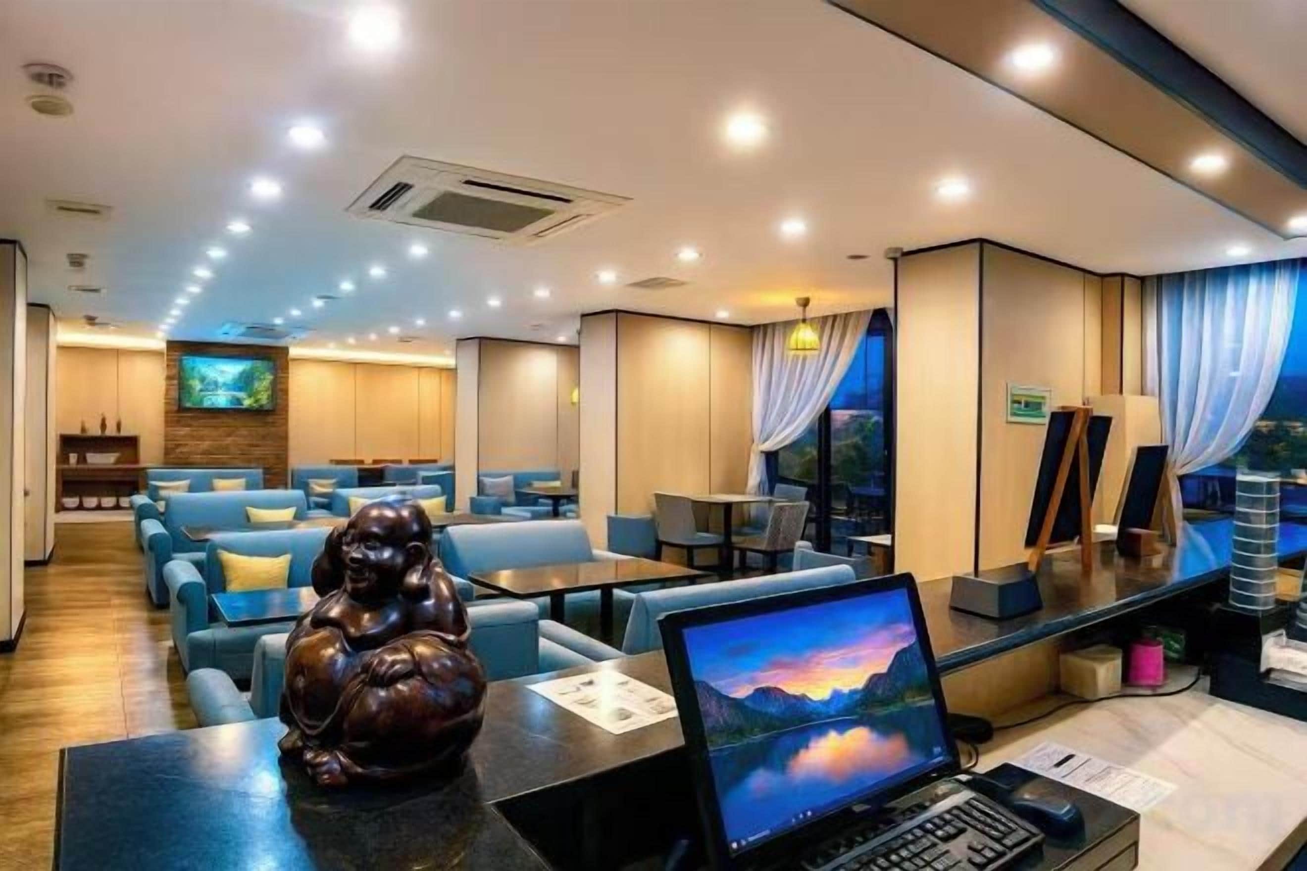 Un moderno vestíbulo de hotel con áreas de descanso, un mostrador de recepción y una pantalla de televisión.
