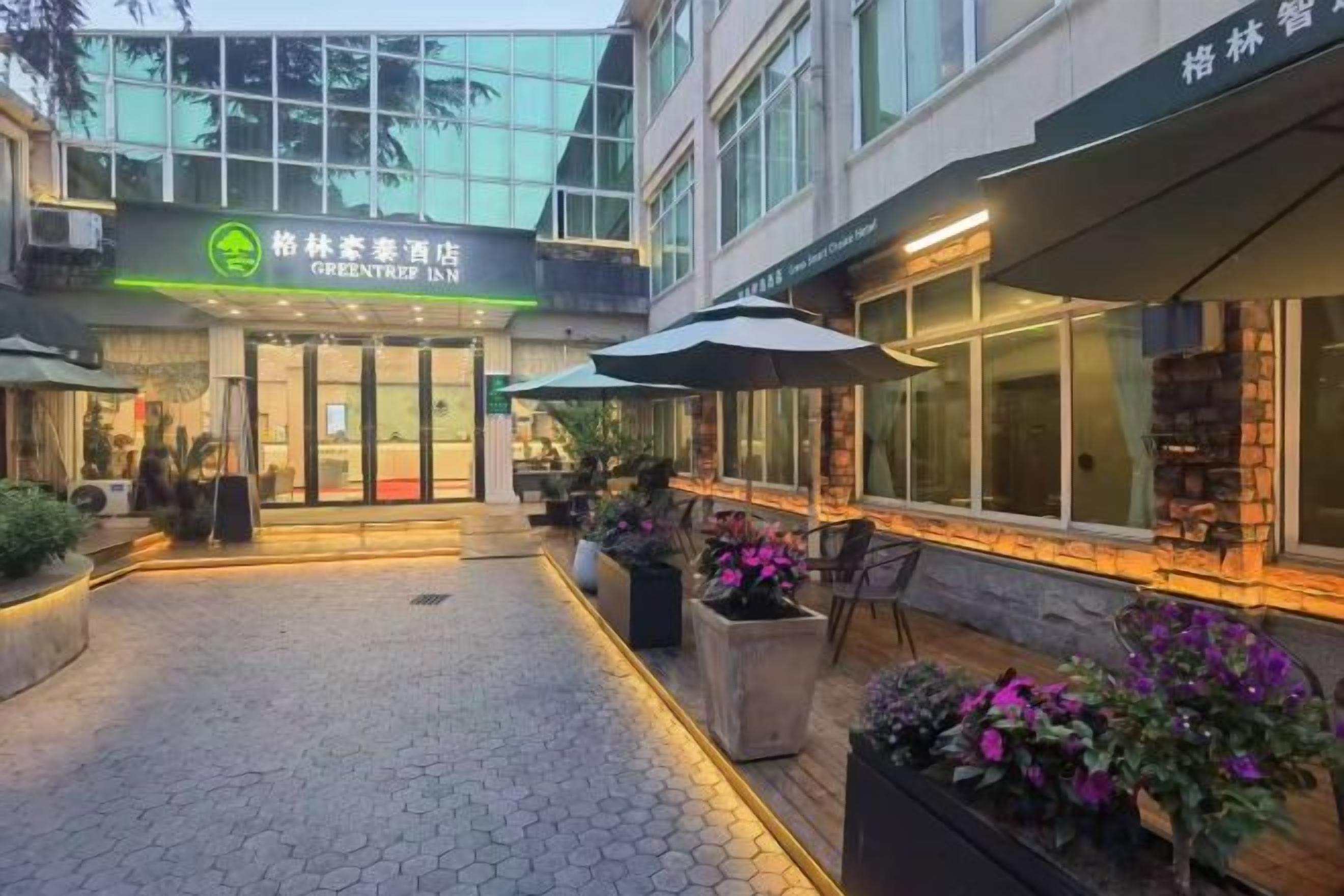 A hotel entrance with a green sign, outdoor seating, and potted plants.