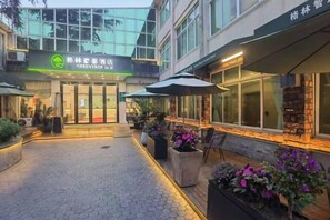 A hotel entrance with a green sign, outdoor seating, and potted plants. - GreenTree Hotel (Shanghai Baotown Pier Normal University Affiliated Zhengda Middle School) (Shanghai)