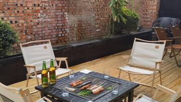 An outdoor dining area with a brick wall, wooden deck, and metal grill.