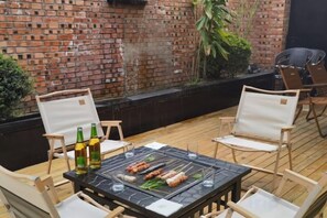 An outdoor dining area with a brick wall, wooden deck, and metal grill. - GreenTree Hotel (Shanghai Baotown Pier Normal University Affiliated Zhengda Middle School) (Shanghai)