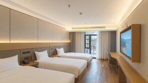 Ein Hotelzimmer mit zwei Betten, einem Schreibtisch, einem Fernseher und einem großen Fenster.
