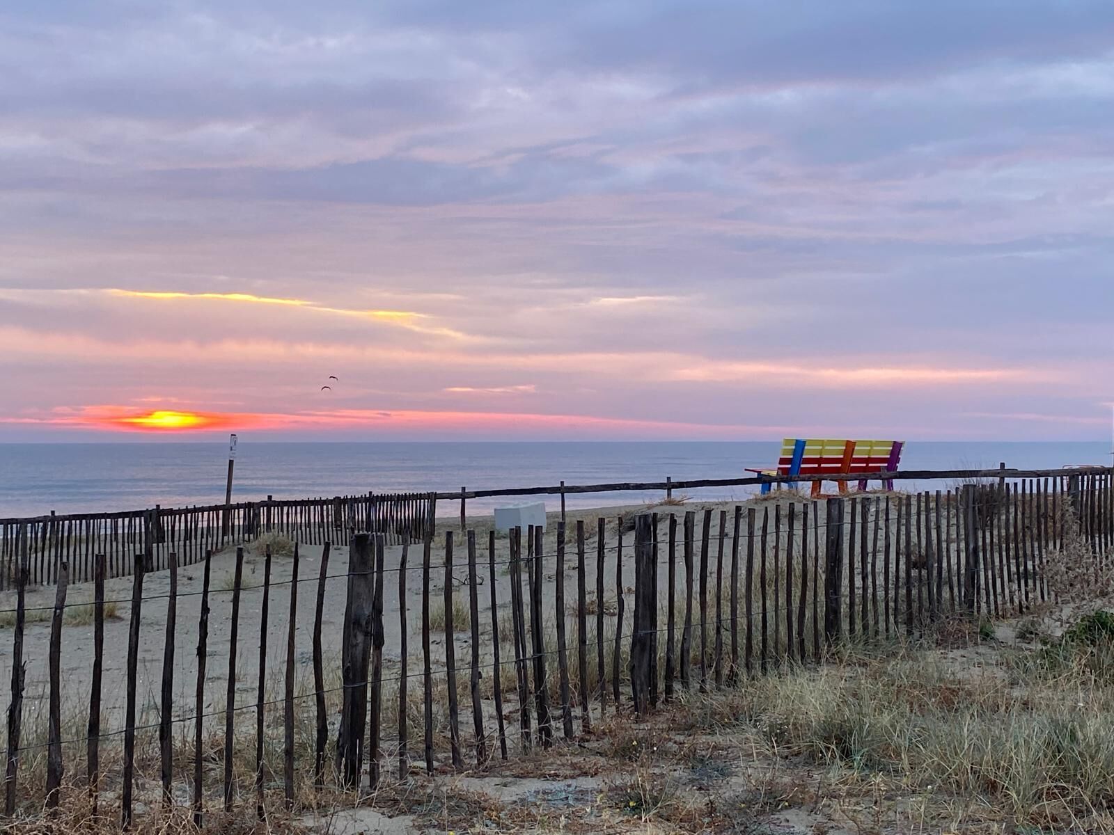 A beach scene with a wooden fence, a colorful beach chair, and the ocean in the background.