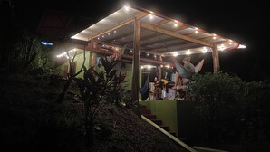 A covered outdoor area with a hammock, steps leading up to a structure, and a small table with items on it.