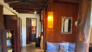 A cozy room with a wooden ceiling, a sofa with patterned cushions, a bookshelf, and a wall-mounted mirror.