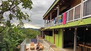 A pool area with a view of the mountains, a covered seating area, and a building with a green facade and string lights.