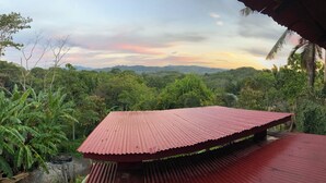 A red metal roofed structure with a view of lush greenery and distant mountains.