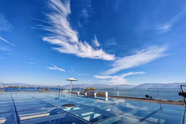 A glass-bottomed infinity pool with a clear view of the mountains and a body of water.