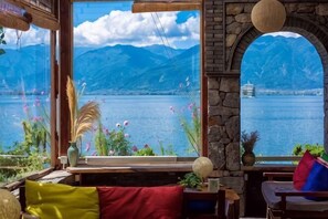 Una habitación con un amplio ventanal que da a un lago y montañas, una pared de piedra y vistas de un crucero.