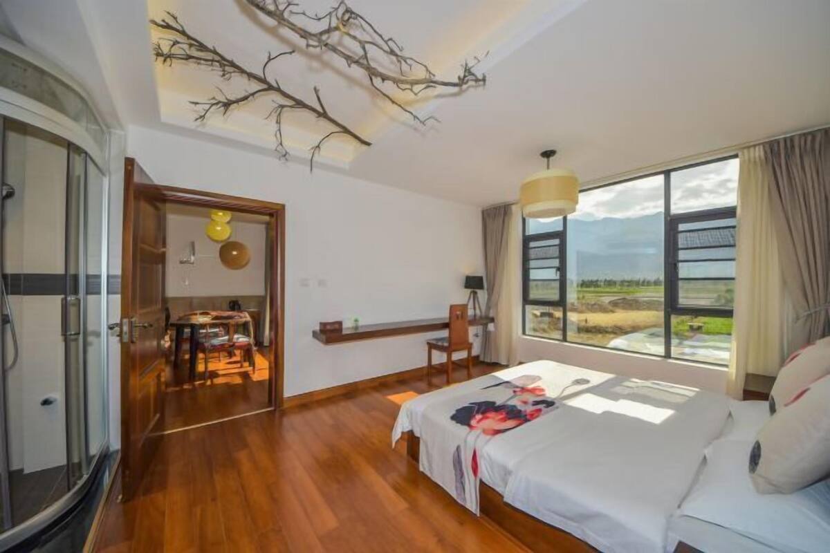 A bedroom with a bed, a desk, a chair, a window with a view, and a ceiling branch decoration.