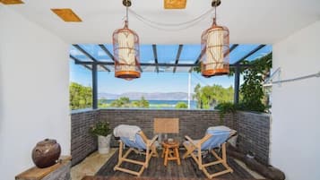 A cozy patio area with wooden flooring, two wicker chairs, a small round table, and hanging lanterns.