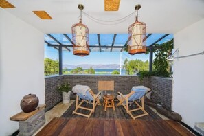 Ein gemütlicher Patio-Bereich mit Holzboden, zwei Korbstühlen, einem kleinen runden Tisch und hängenden Laternen.