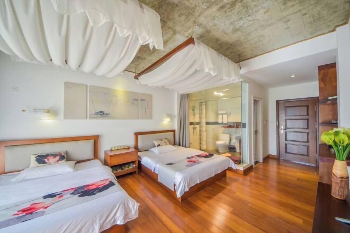 A hotel room with two beds, wooden flooring, a large mirror, and a wooden door.