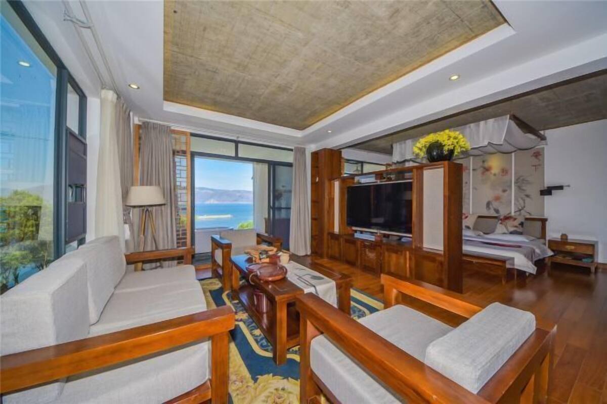 A spacious living area with a large TV, wooden furniture, and a view of the ocean.