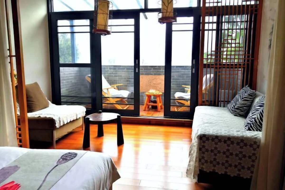 A room with a sofa, a bed, a small table, and a view through a glass door to an outdoor area with chairs and a table.