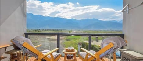 Un balcón con sillas de madera y una mesita, con vistas a un paisaje montañoso.