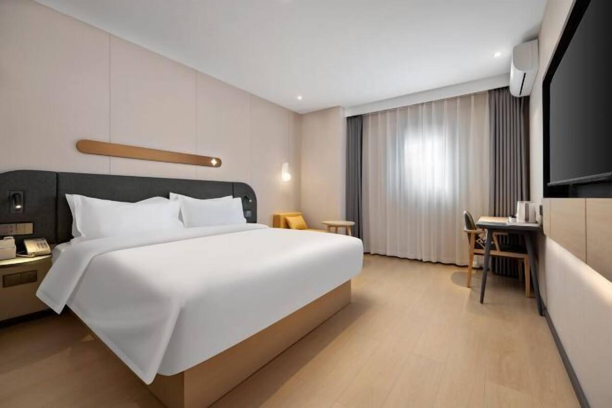 Ein modernes Hotelzimmer mit einem großen Bett, Nachttischen, einem Schreibtisch mit Stuhl und einem großen Fenster mit Vorhängen.