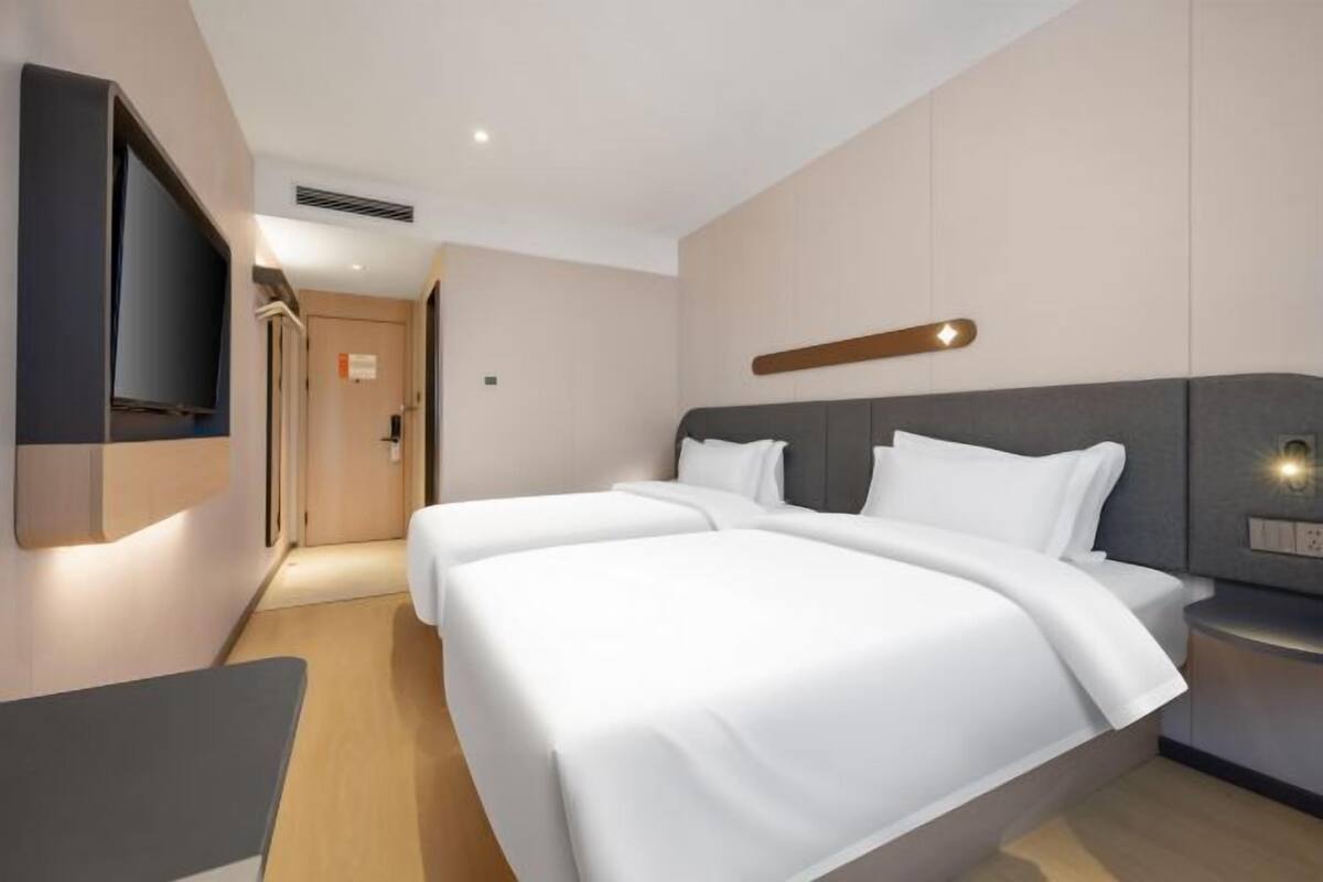 Ein modernes Hotelzimmer mit zwei Betten, einem an der Wand befestigten Flachbildfernseher, einem Nachttisch und Holzboden.