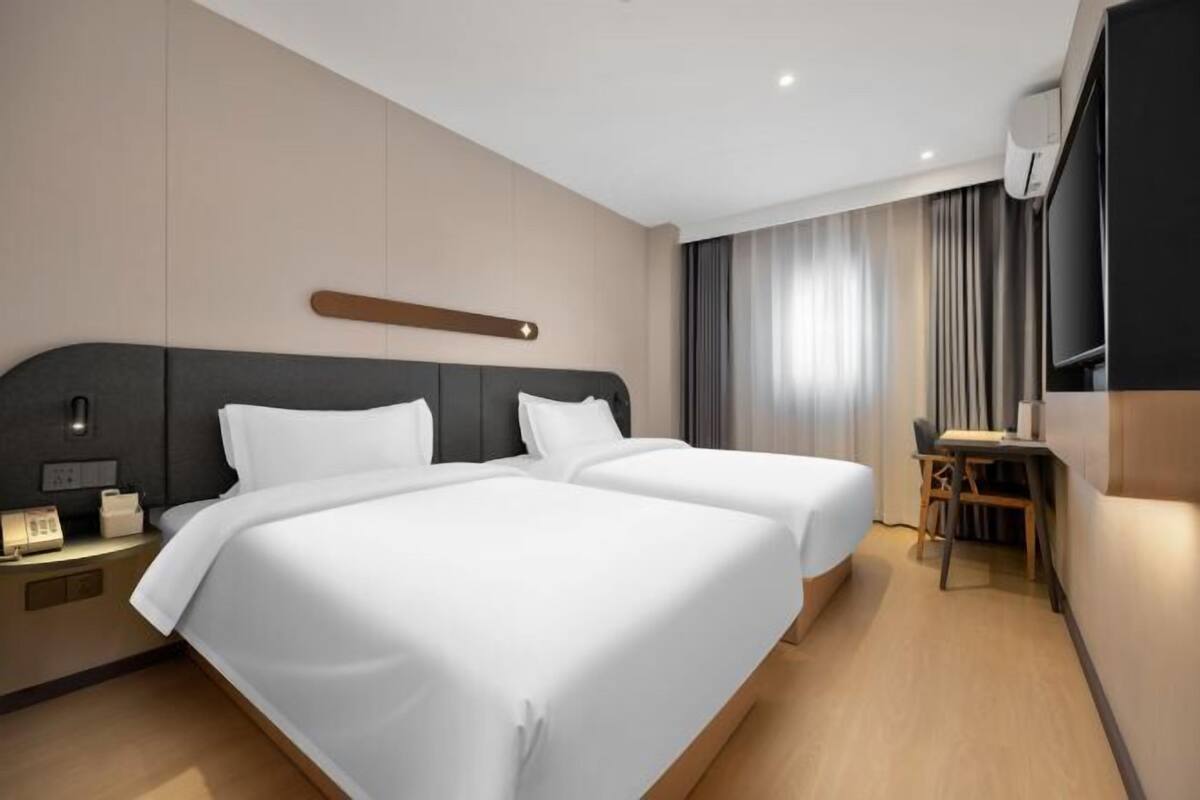Ein Hotelzimmer mit zwei Betten, einem Schreibtisch, einem Stuhl, einem Fernseher und einem Fenster mit Vorhängen.