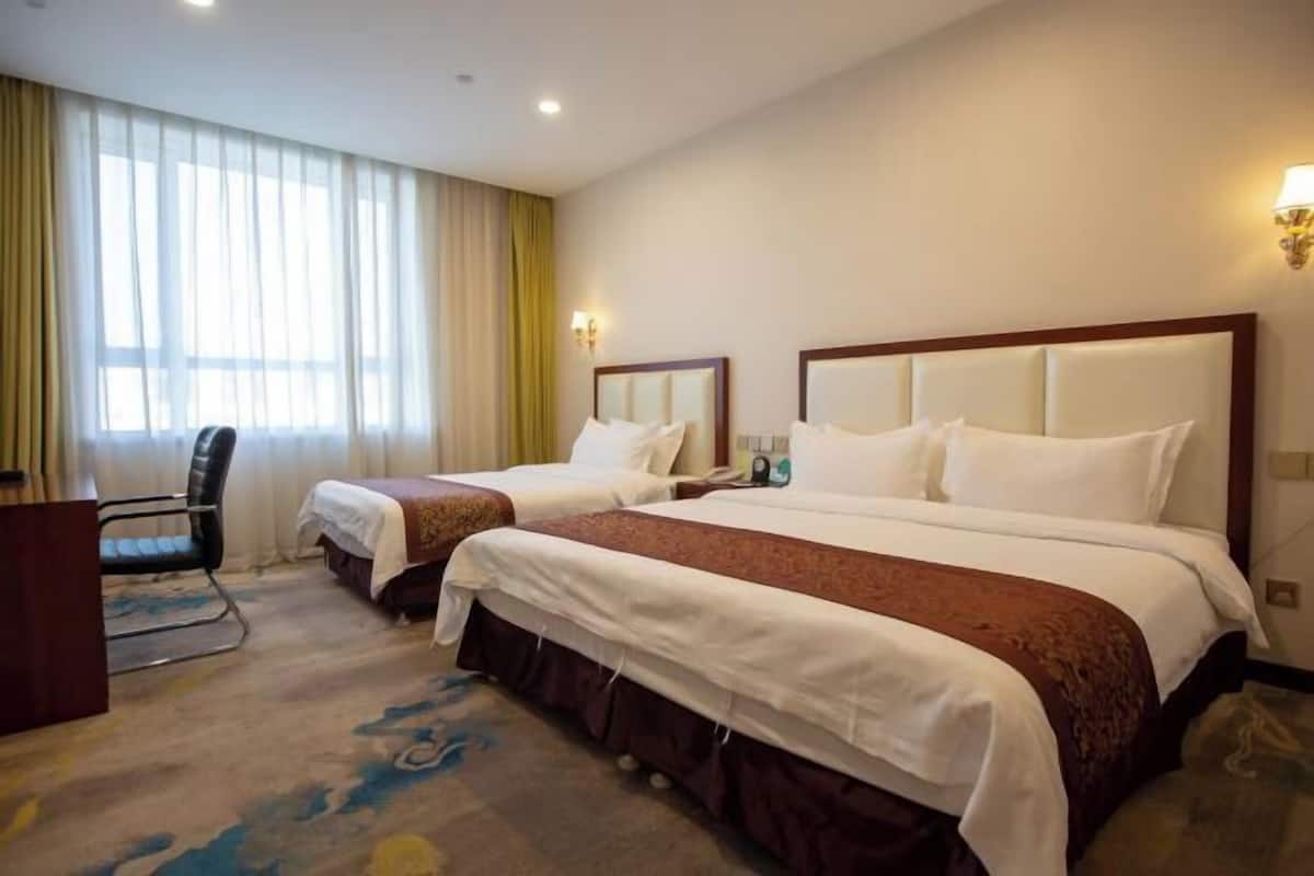 A hotel room with two beds, a desk, a chair, and a large window with curtains.