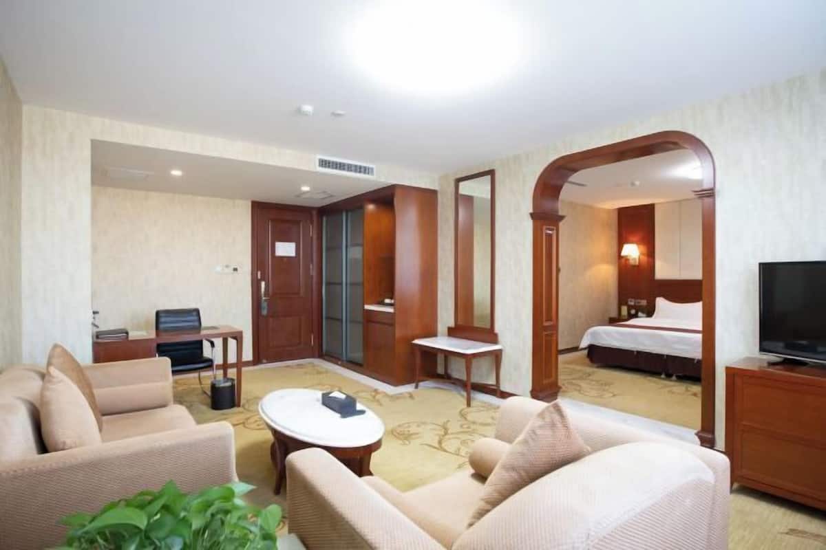 A hotel room with a sofa, armchair, small table, TV, and a bed.