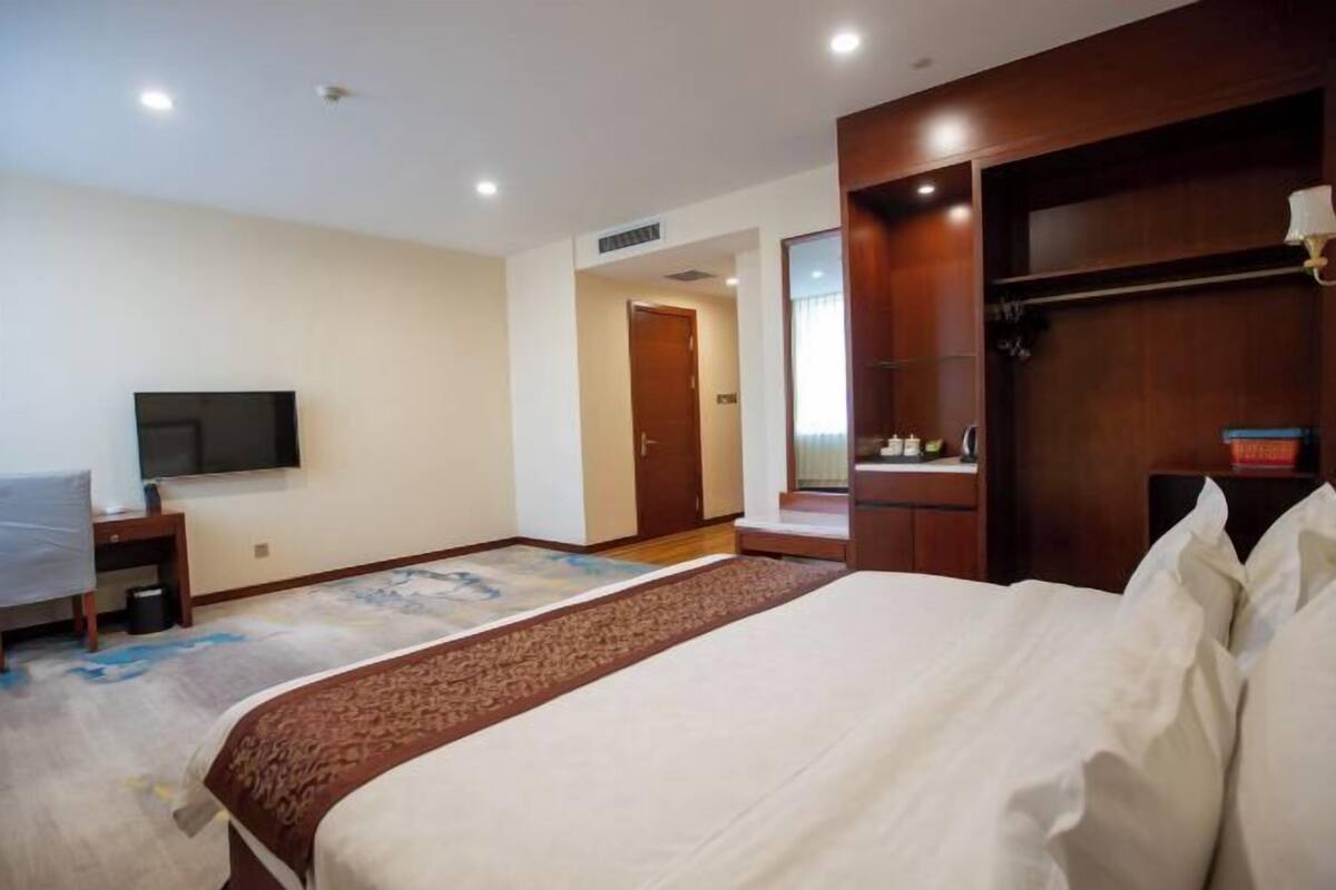 A hotel room with a large bed, a television, a desk, and a wardrobe.