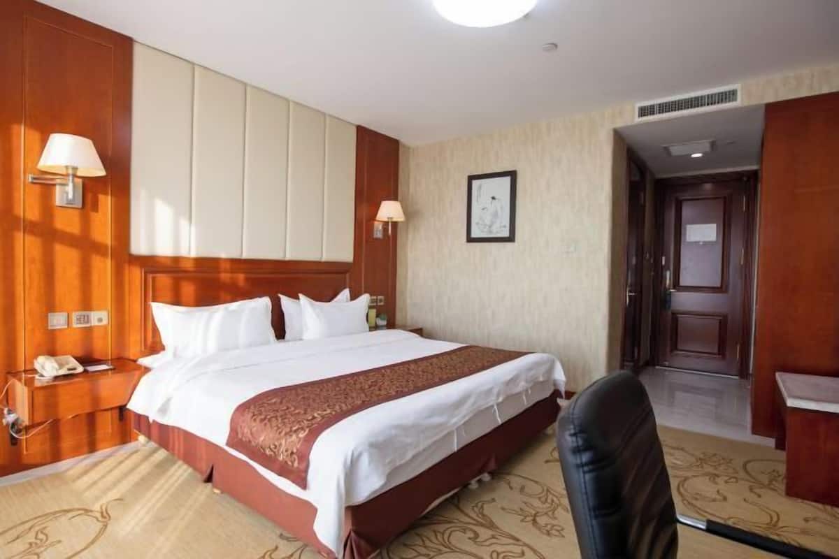 A hotel room with a large bed, wooden paneling, a desk with a lamp, and a chair.