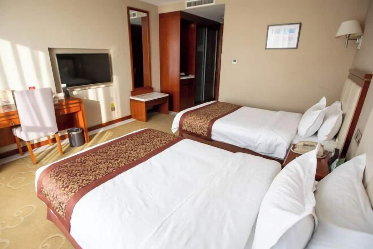 A hotel room with two beds, a desk with a chair, a television, and a wardrobe.