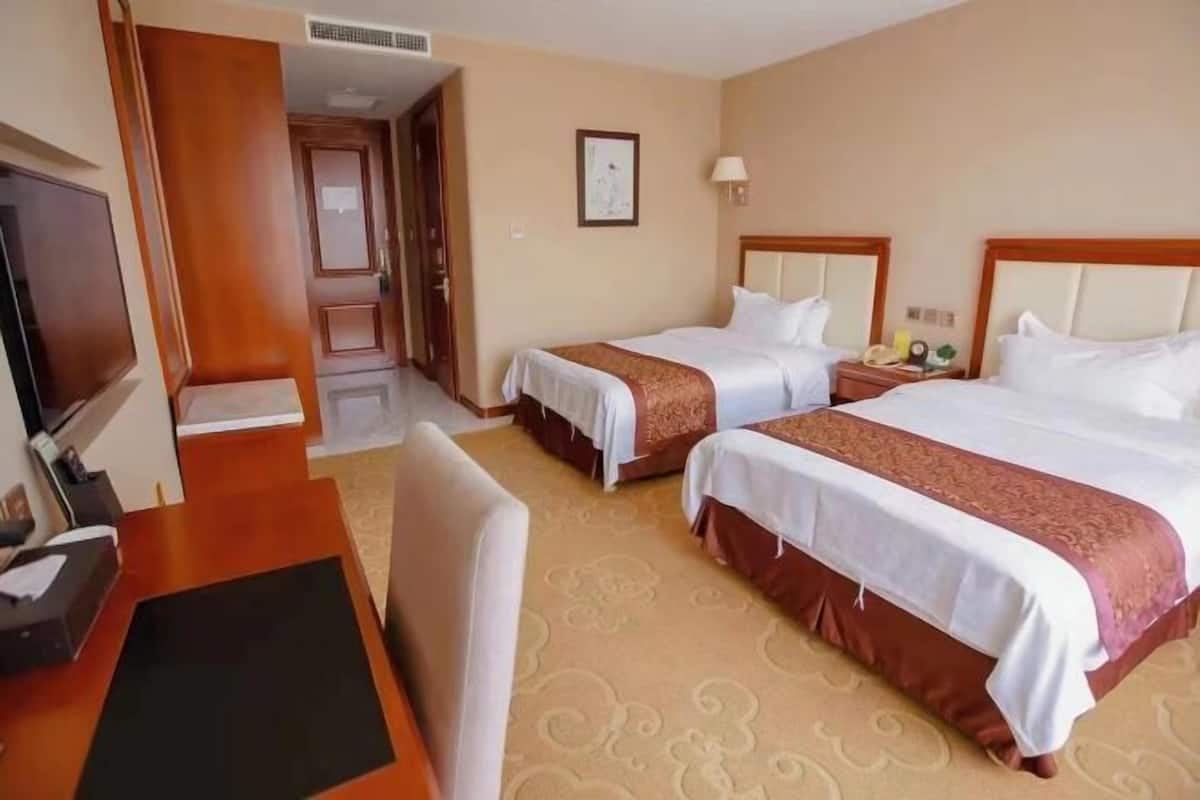 A hotel room with two beds, a desk, a television, and a door leading to another room.