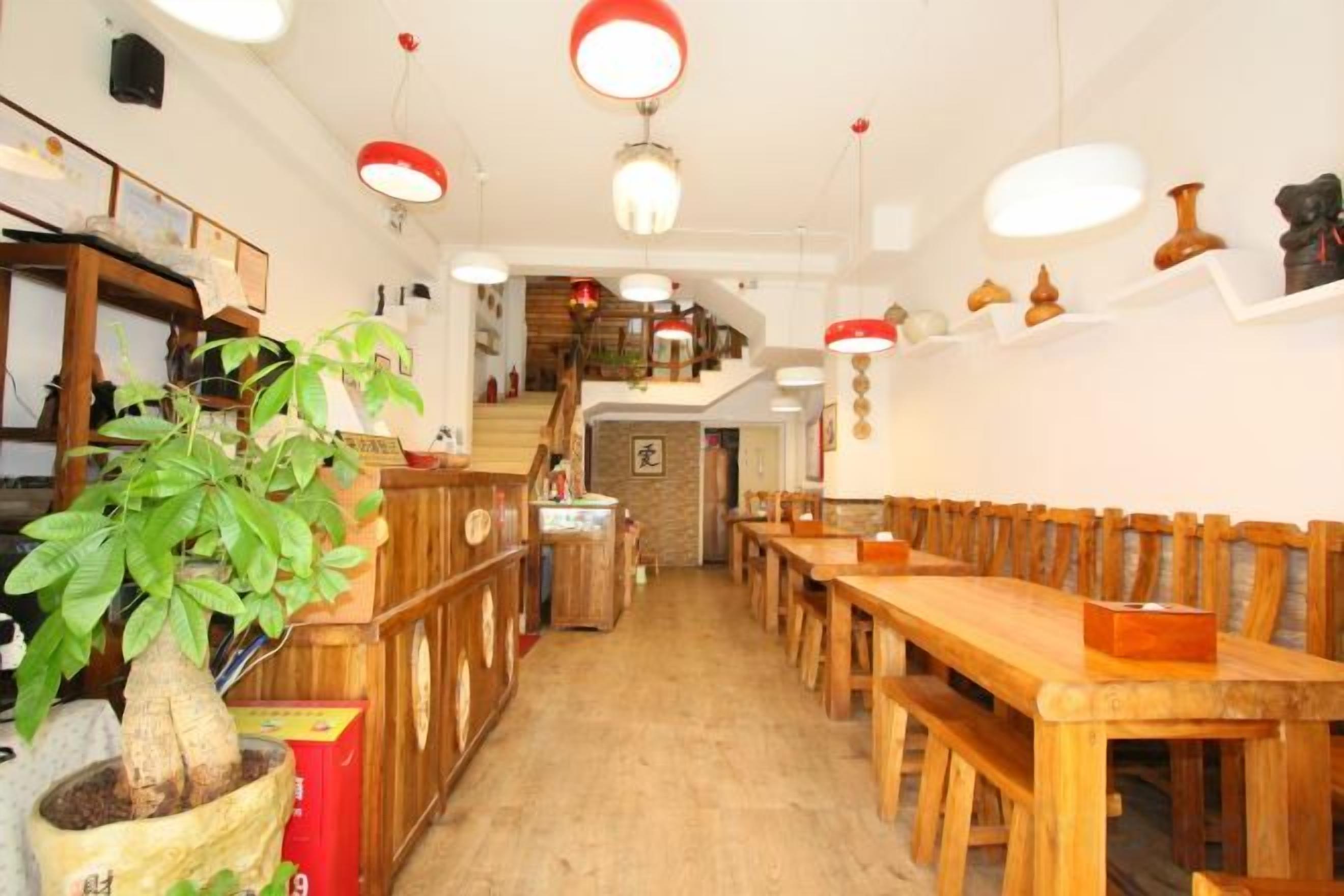 A restaurant interior with wooden tables and chairs, a potted plant, and hanging red lamps.