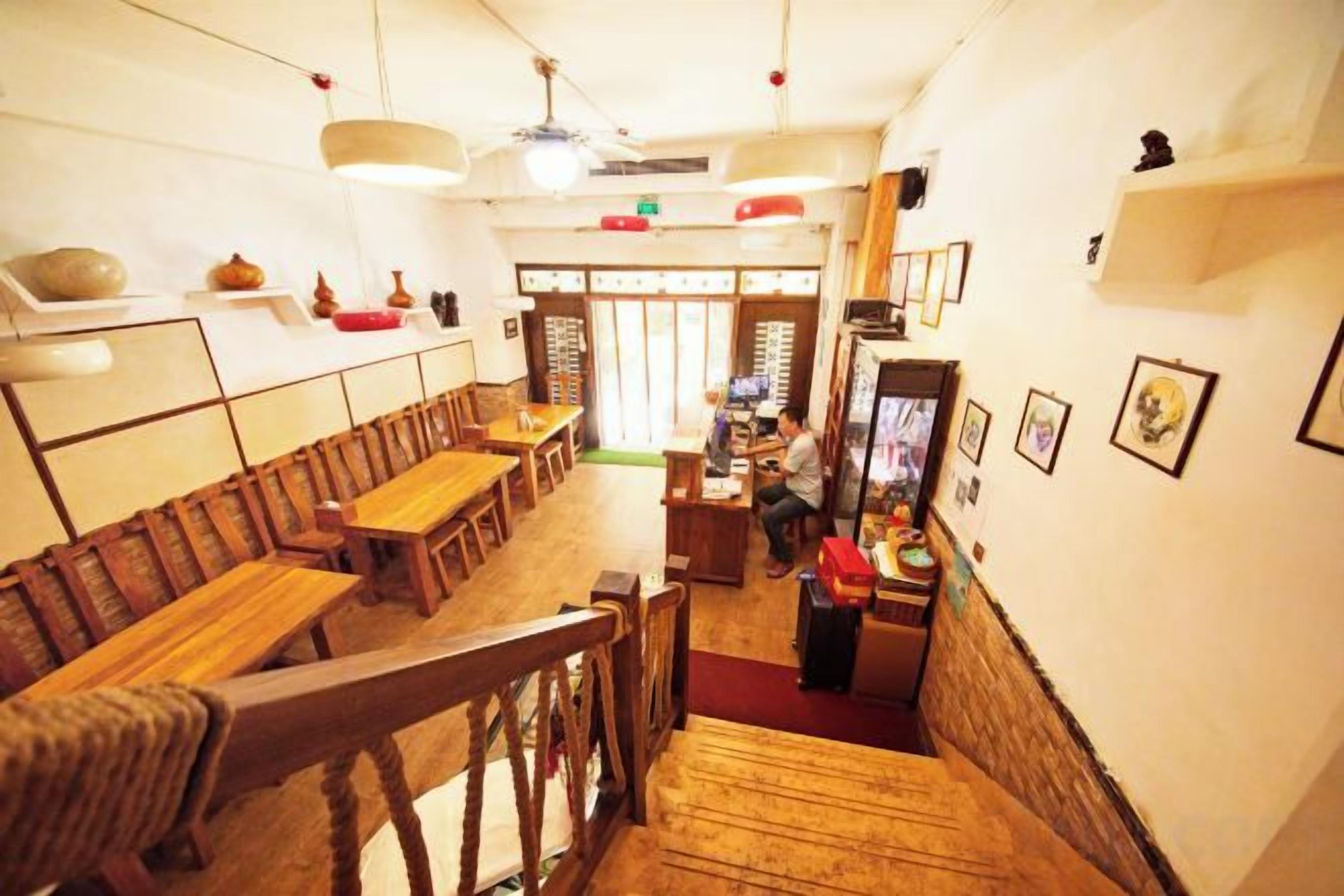 A restaurant interior with wooden tables and chairs, a counter, and a staircase.