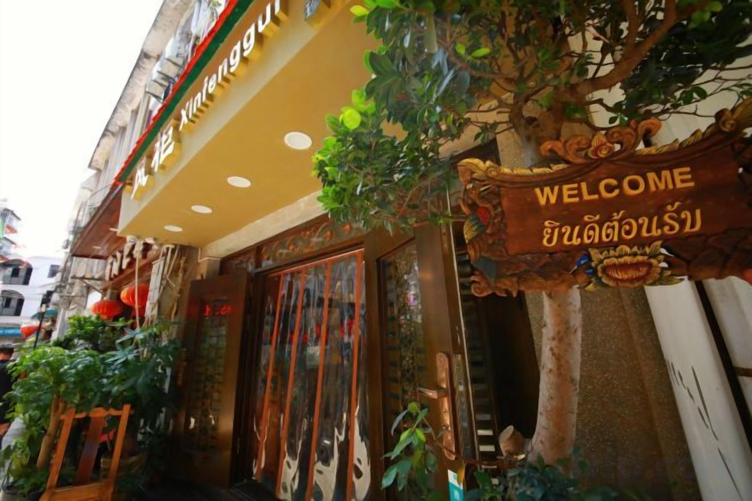 A hotel entrance with a traditional Thai sign, a wooden door, and potted plants.